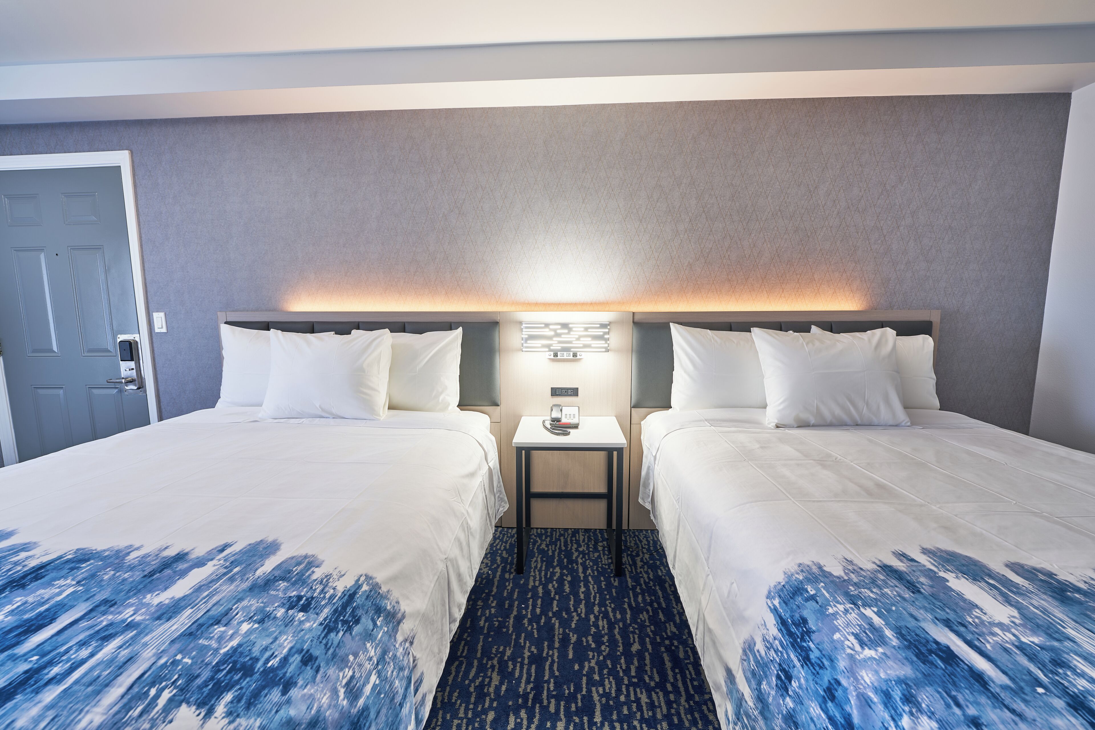 Een hotelkamer met twee bedden, een nachtkastje en een wandlamp.
