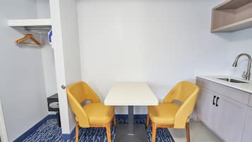 A compact kitchen with a white table and two yellow chairs, a sink, and a small cabinet.