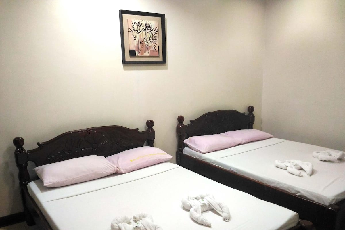 Zwei Holzbetten mit weißen Laken und rosa Kissen, ein gerahmtes Kunstwerk an der Wand und ein Handtuch auf dem Boden.