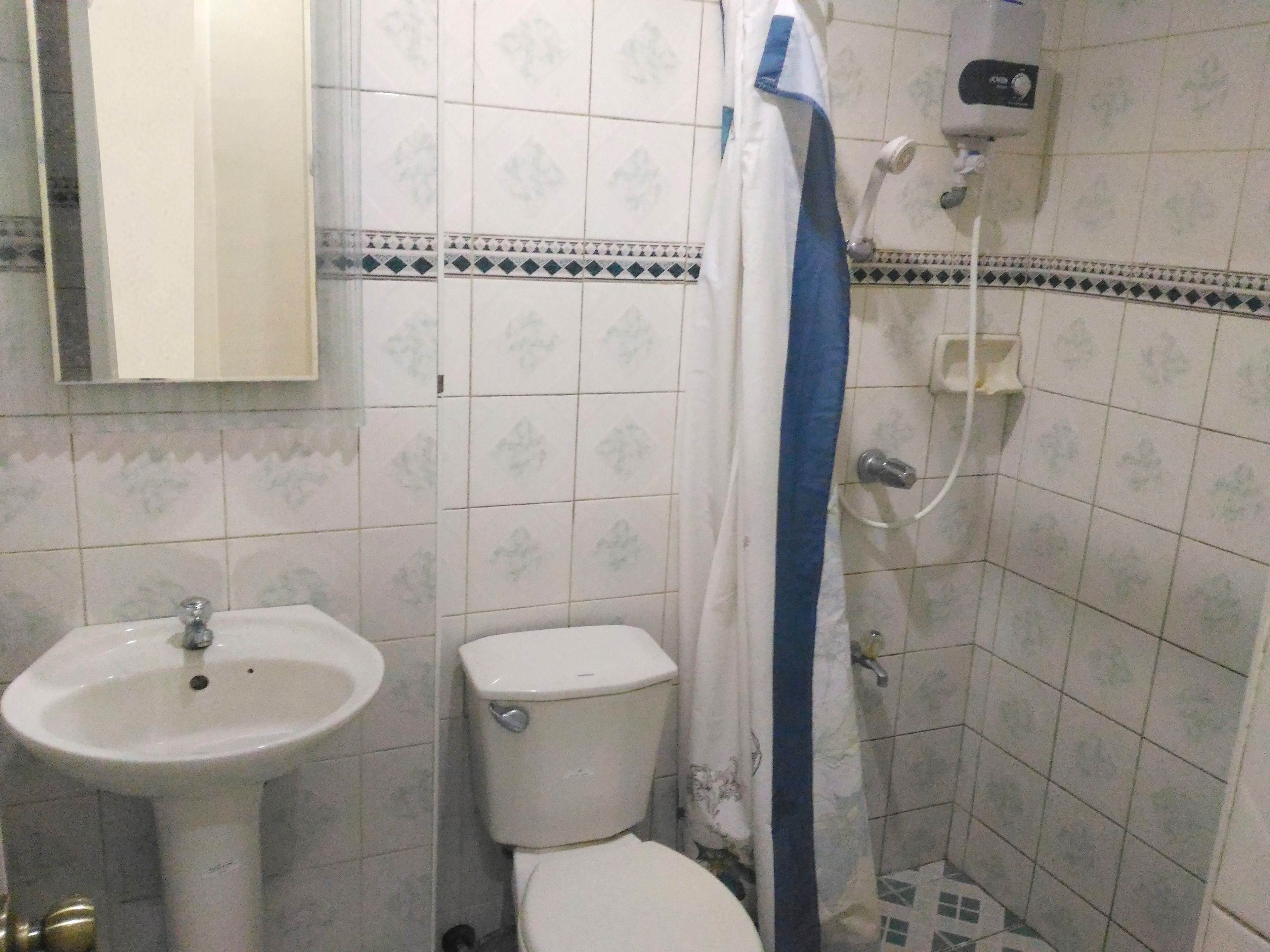 Um banheiro com pia branca, vaso sanitário e chuveiro. Há um espelho acima da pia e um box de vidro com uma faixa azul.