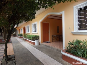 A row of yellow buildings with white trim, each with a door and window. There are potted plants and a bench outside. - Tubod Flowing Waters Resort (Talisay)