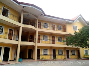 A multi-story building with balconies, numbered doors, and a small trash bin. - Tubod Flowing Waters Resort (Talisay)
