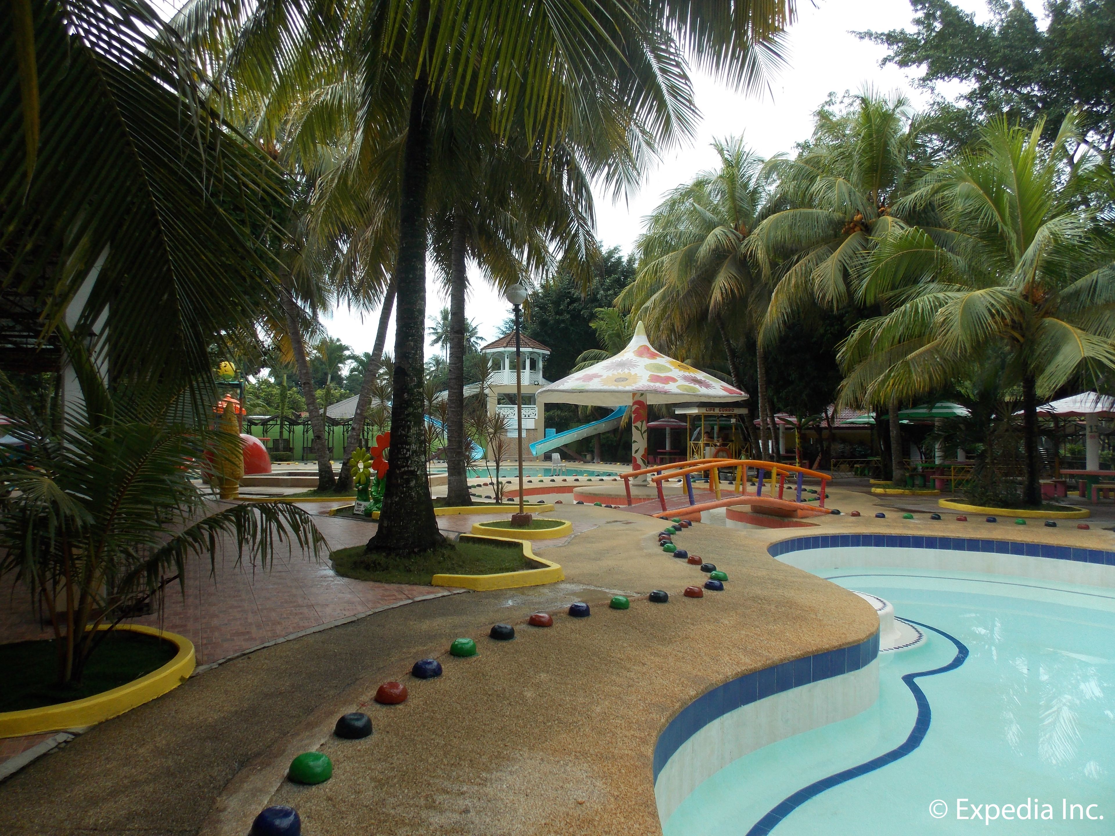 Un espace piscine doté d’un toboggan aquatique, de palmiers et d’une aire de jeux pour enfants.