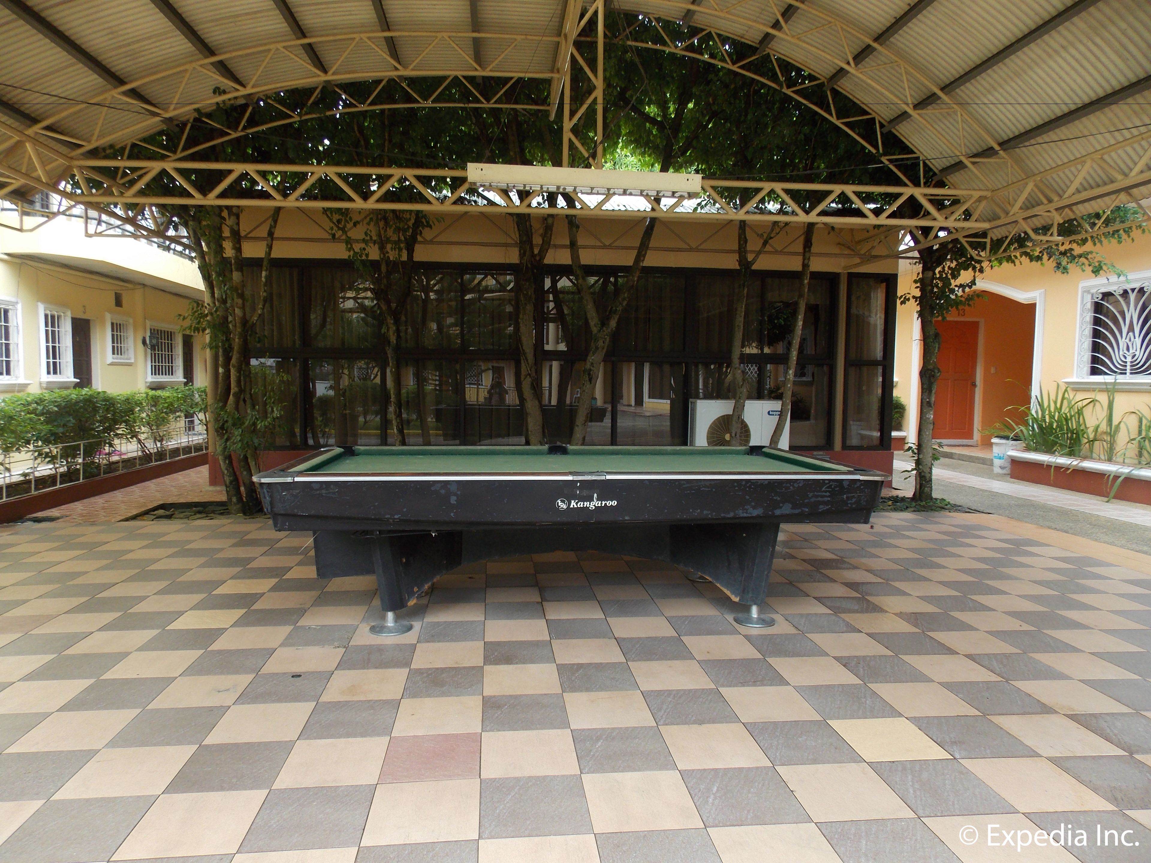 A pool table under a covered area with a checkered floor, surrounded by trees and buildings.