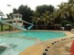 A swimming pool with a water slide, palm trees, and lounge chairs. - Tubod Flowing Waters Resort (Talisay)