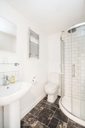 Un baño con lavamanos blanco, inodoro y ducha con mampara de vidrio.