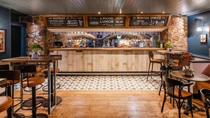 Una zona de bar con mostrador de madera, taburetes y una pizarra con la carta.