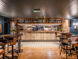 Una zona de bar con mostrador de madera, taburetes y una pizarra con la carta.