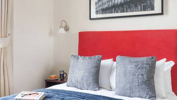 Habitación de hotel con cabecera roja, almohadas grises, manta azul y un cuadro en la pared.