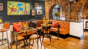 Un rincón de bar acogedor con pared de piedra, mostrador de bar de madera y una disposición de asientos que incluye un sofá y varias sillas.
