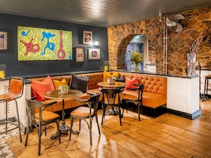Un rincón de bar acogedor con pared de piedra, mostrador de bar de madera y una disposición de asientos que incluye un sofá y varias sillas.