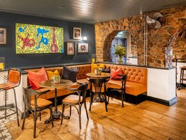 Un rincón de bar acogedor con pared de piedra, mostrador de bar de madera y una disposición de asientos que incluye un sofá y varias sillas.