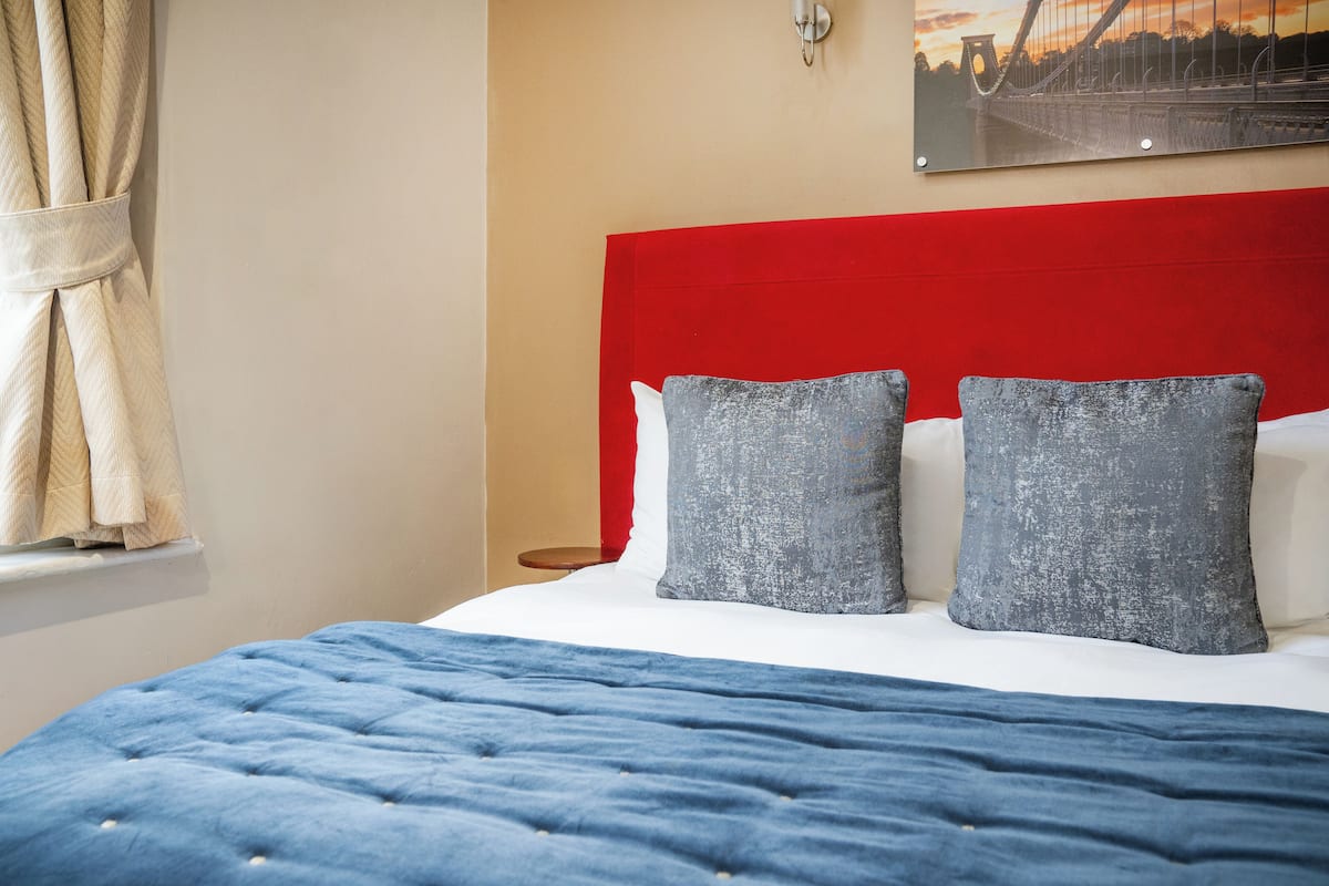 A bed with a red headboard, two grey pillows, and a blue bedspread.