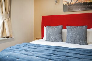 Una cama con cabecera roja, dos almohadas grises y una colcha azul.