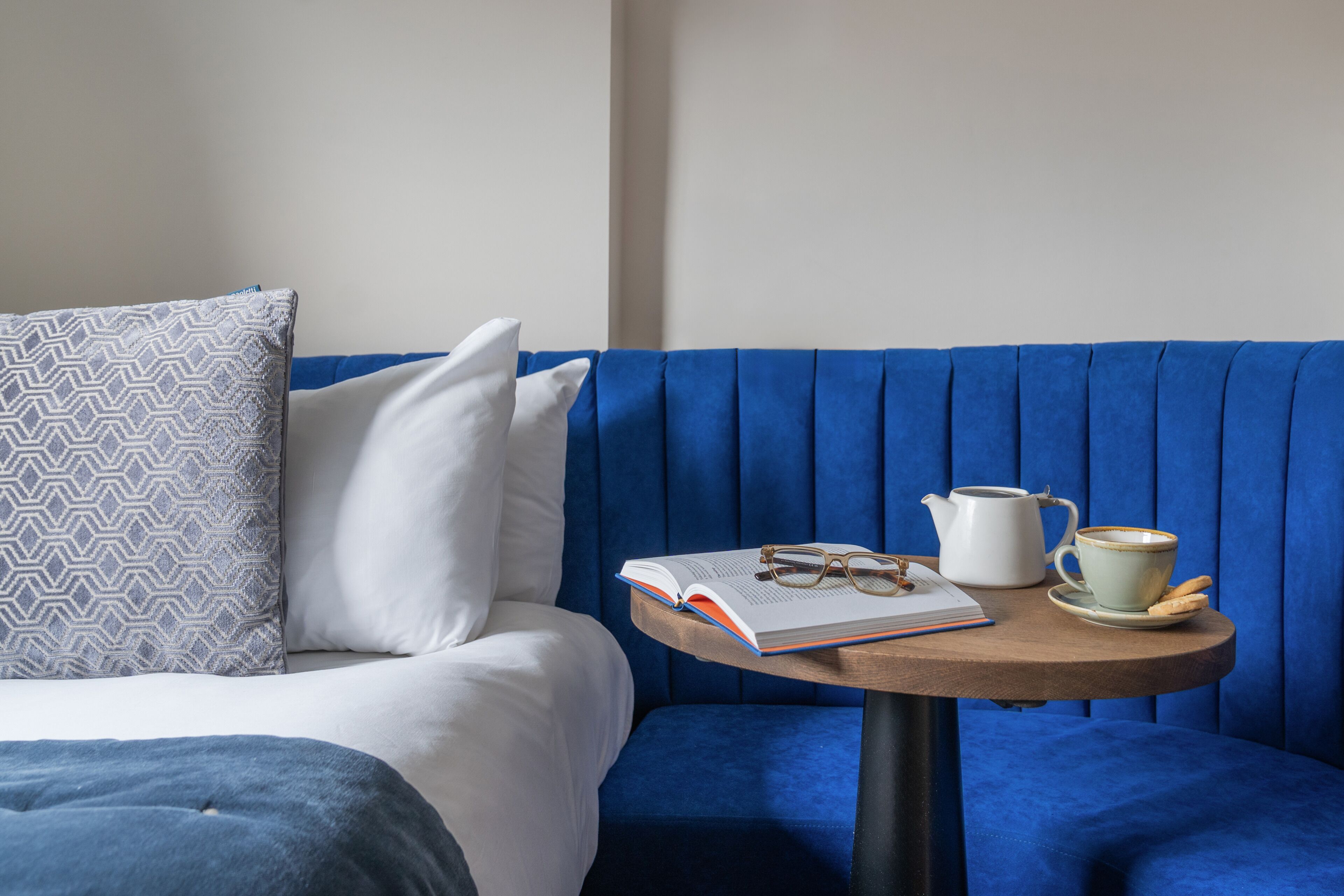 A room with a blue sofa, a small round table with a book, glasses, a teapot, and a cup.