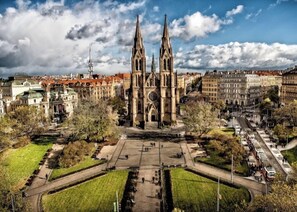 A cathedral with twin spires, surrounded by a square plaza with a fountain, and a tram line running parallel to the building. - Hotel Claris (Prague)
