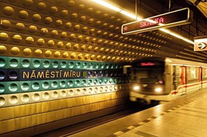 A subway station with a train approaching, signs indicating directions, and a wall with circular patterns and text. - Hotel Claris (Prague)