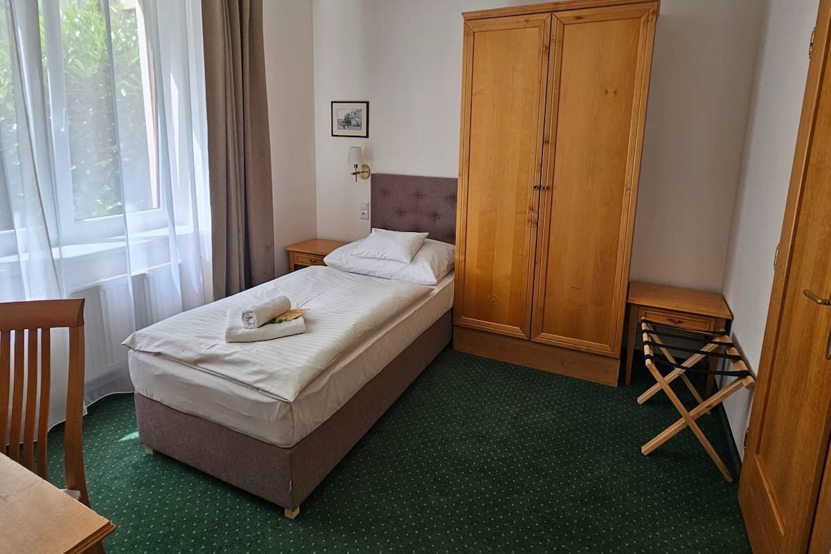 Une chambre d’hôtel avec un lit, une armoire en bois, une petite table, une chaise et une fenêtre avec des rideaux.