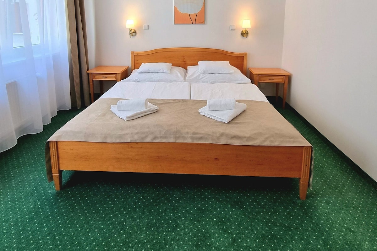 Une chambre d’hôtel avec un grand lit, deux tables de chevet, un tableau au mur et deux lampes fixées au mur.