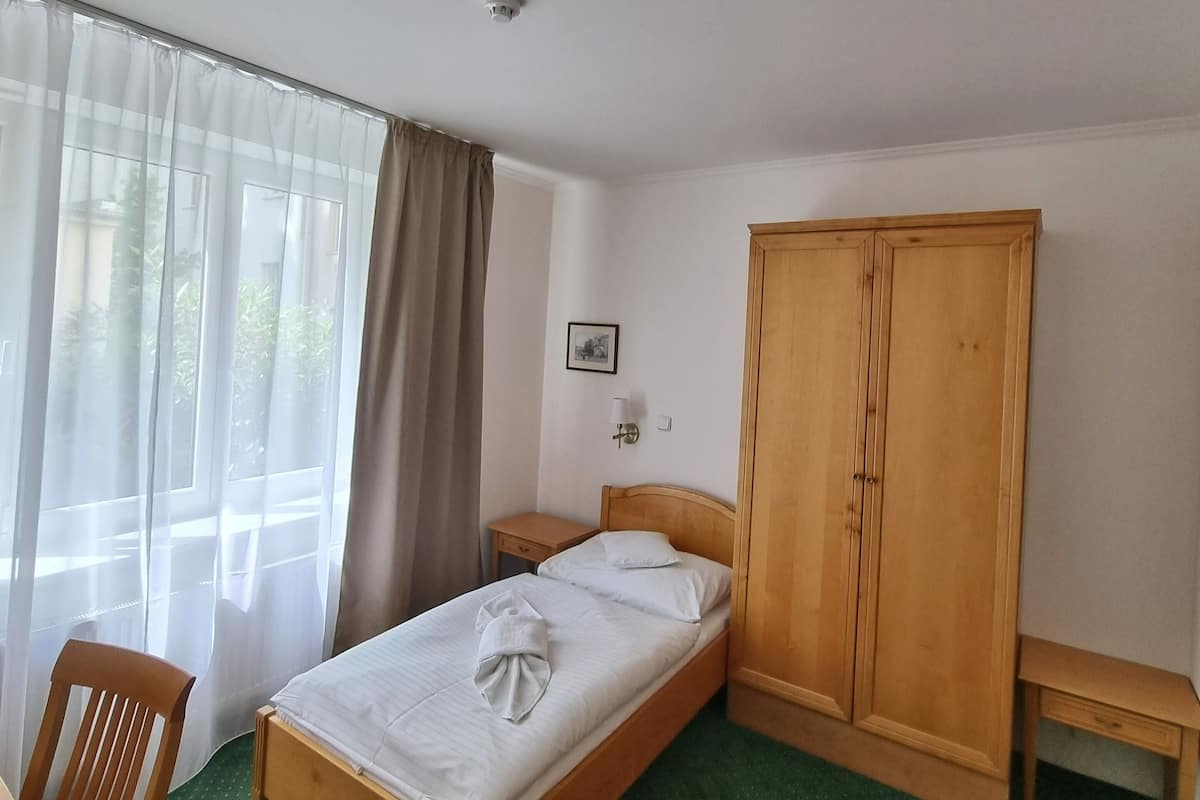 Une chambre d’hôtel bien rangée, avec un lit simple, une armoire en bois, une petite table de chevet et une chaise.