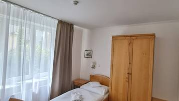 Habitación de hotel ordenada con una cama individual, un armario de madera, una mesita de noche pequeña y una silla.