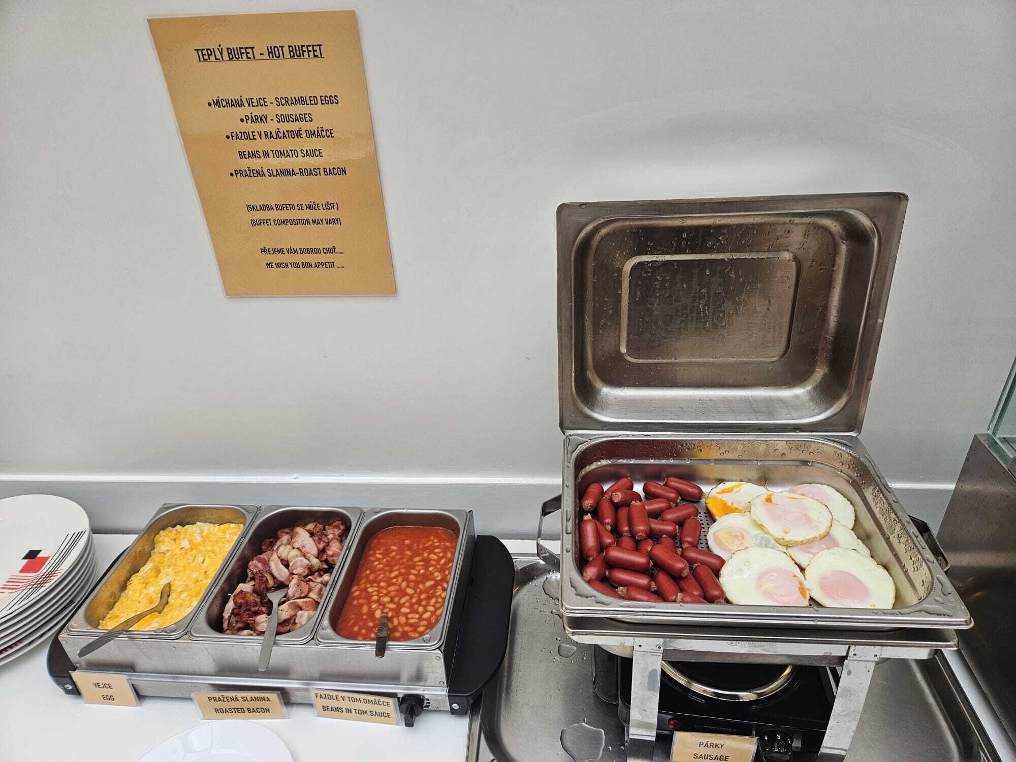 A buffet with labeled food options including scrambled eggs, sausages, beans in tomato sauce, and roast bacon.