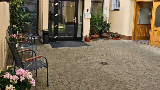 A hotel entrance with a glass door, outdoor seating with chairs and tables, and potted plants. - Hotel Claris (Prague)