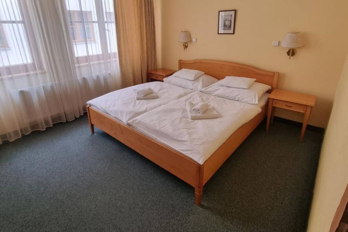 Un lit double bien fait, avec du linge de lit blanc, deux tables de chevet avec des lampes et une fenêtre ornée de rideaux légers.