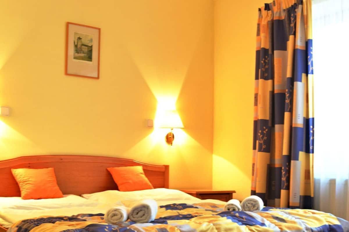 Une chambre d’hôtel avec un lit, une lampe fixée au mur, un tableau encadré et une fenêtre avec des rideaux.