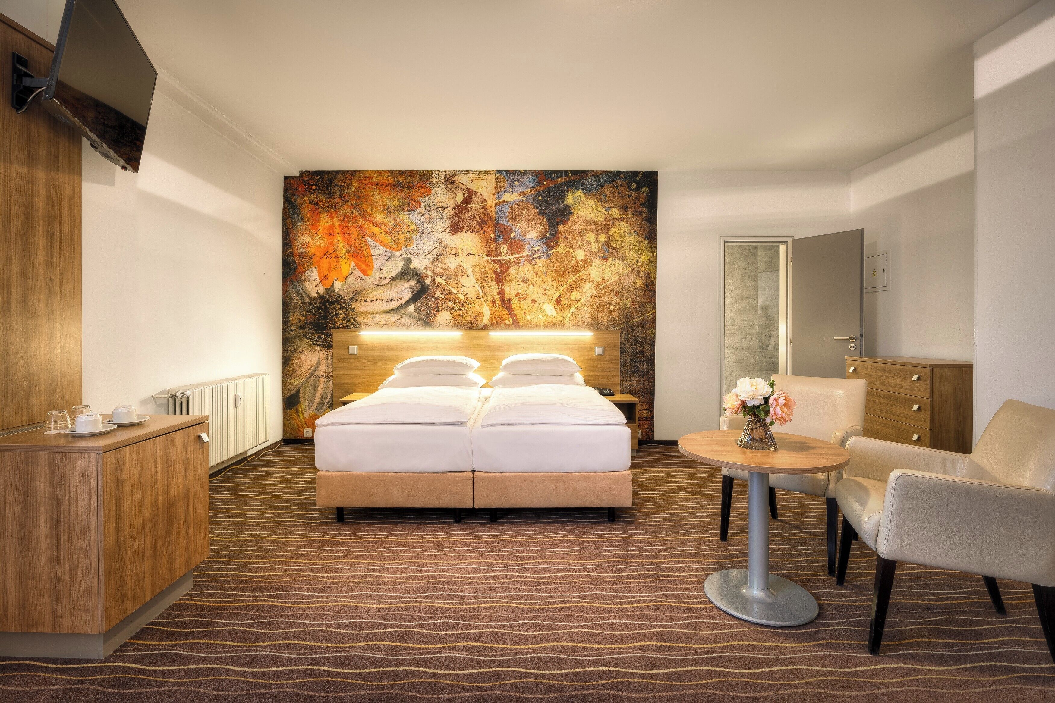 A hotel room with a large bed, a desk, a chair, and a wall-mounted TV.