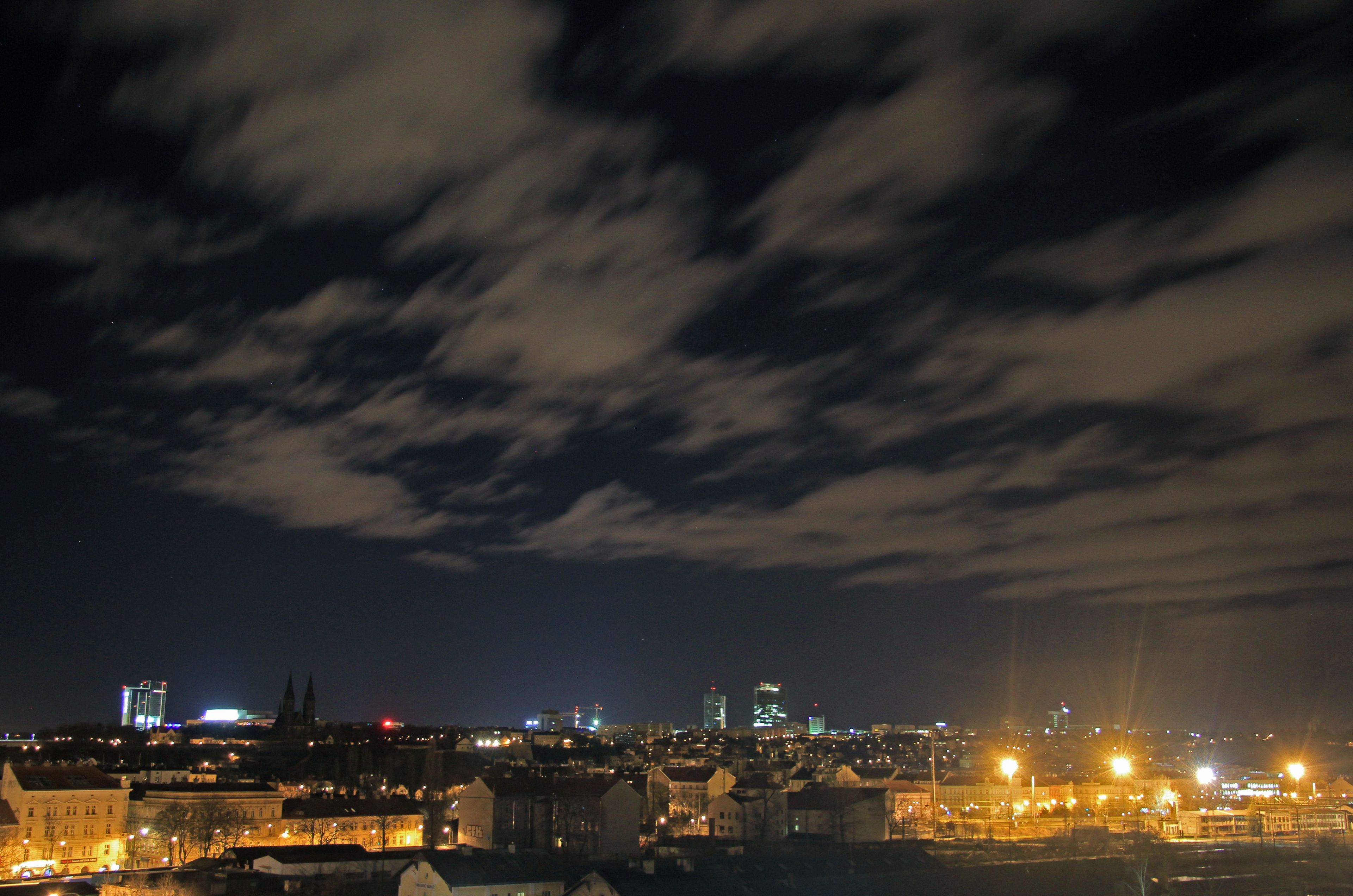 A nighttime cityscape with illuminated buildings and a cloudy sky.