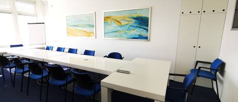 Un salón de conferencias con una larga mesa, sillas azules y dos cuadros abstractos en la pared.