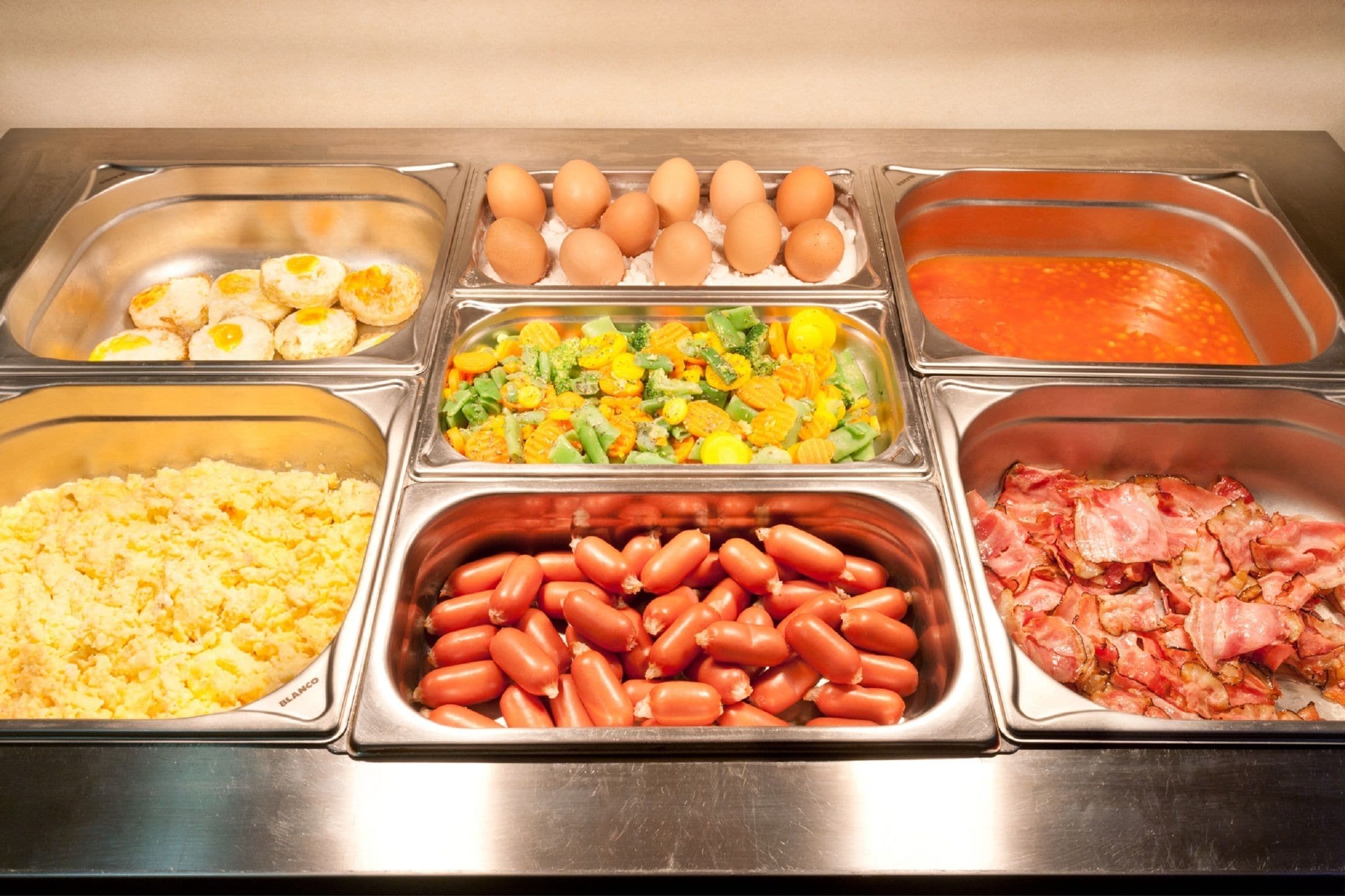 Ein reichhaltiges Buffet mit verschiedenen Speisen, darunter Eier, Würstchen und Schinken.