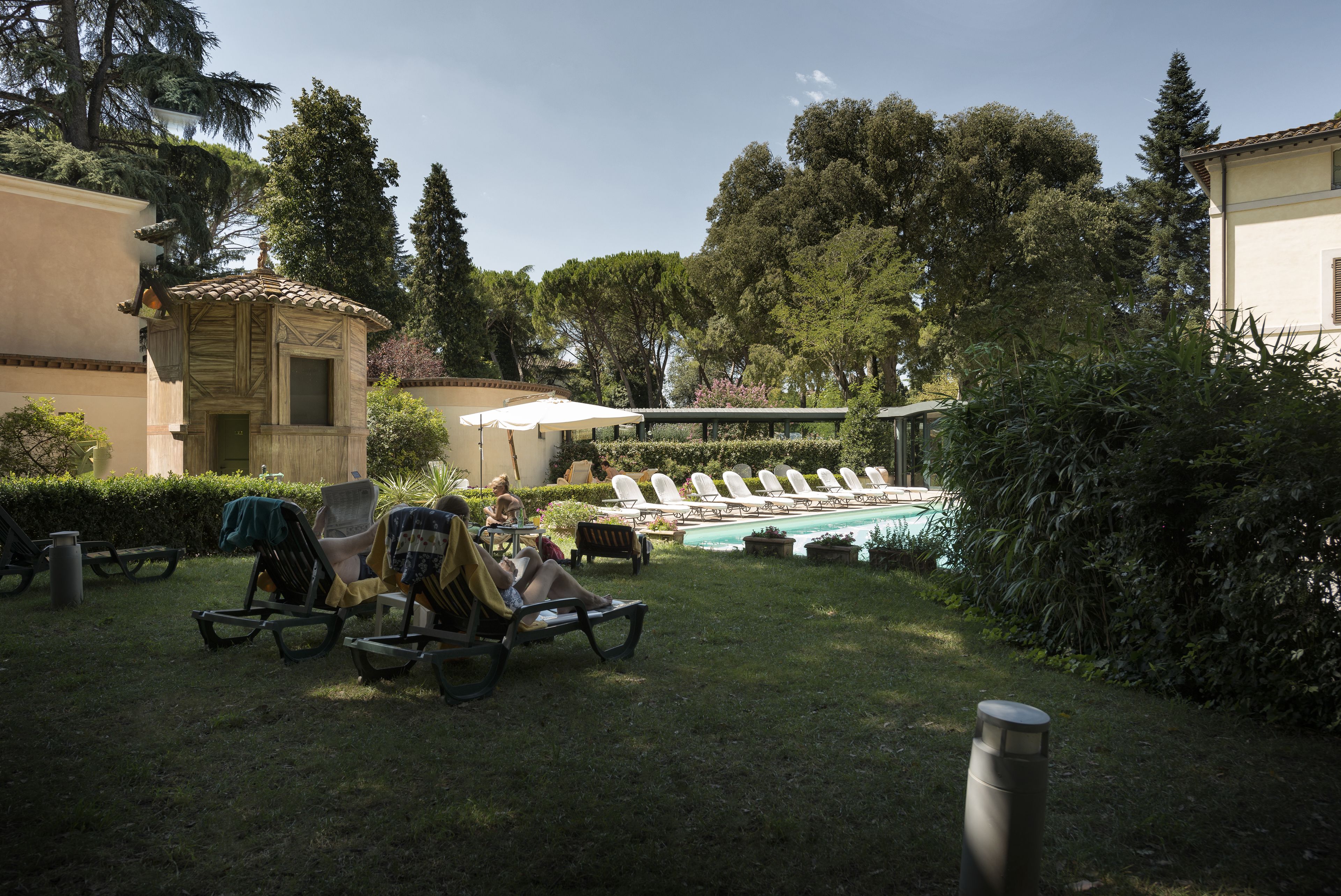 Un espace aménagé au bord de la piscine, avec des chaises longues, un petit kiosque et une pergola dotée de parasols.