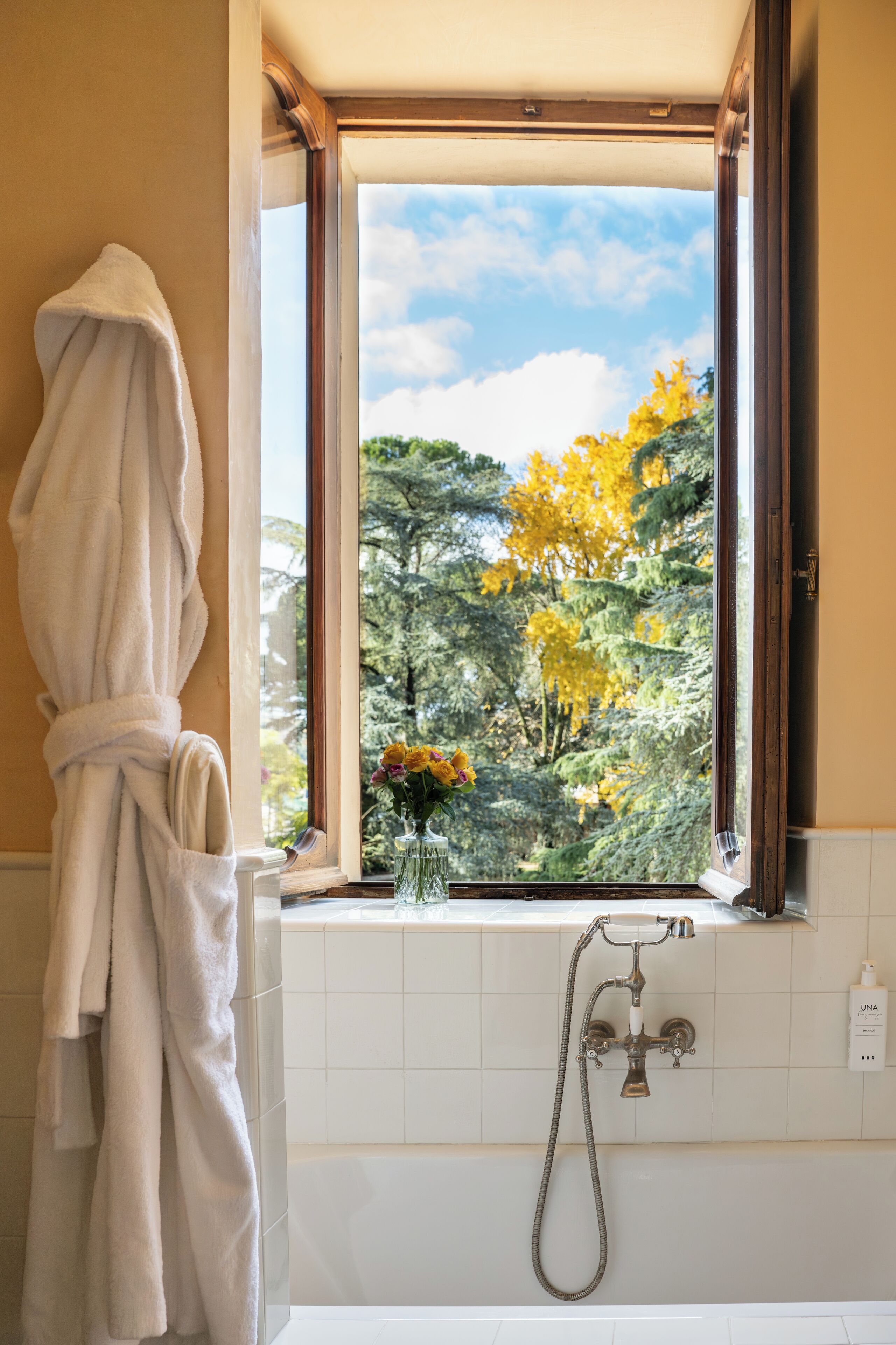 Une salle de bain avec une baignoire, une fenêtre donnant sur la verdure et une serviette blanche accrochée au mur.