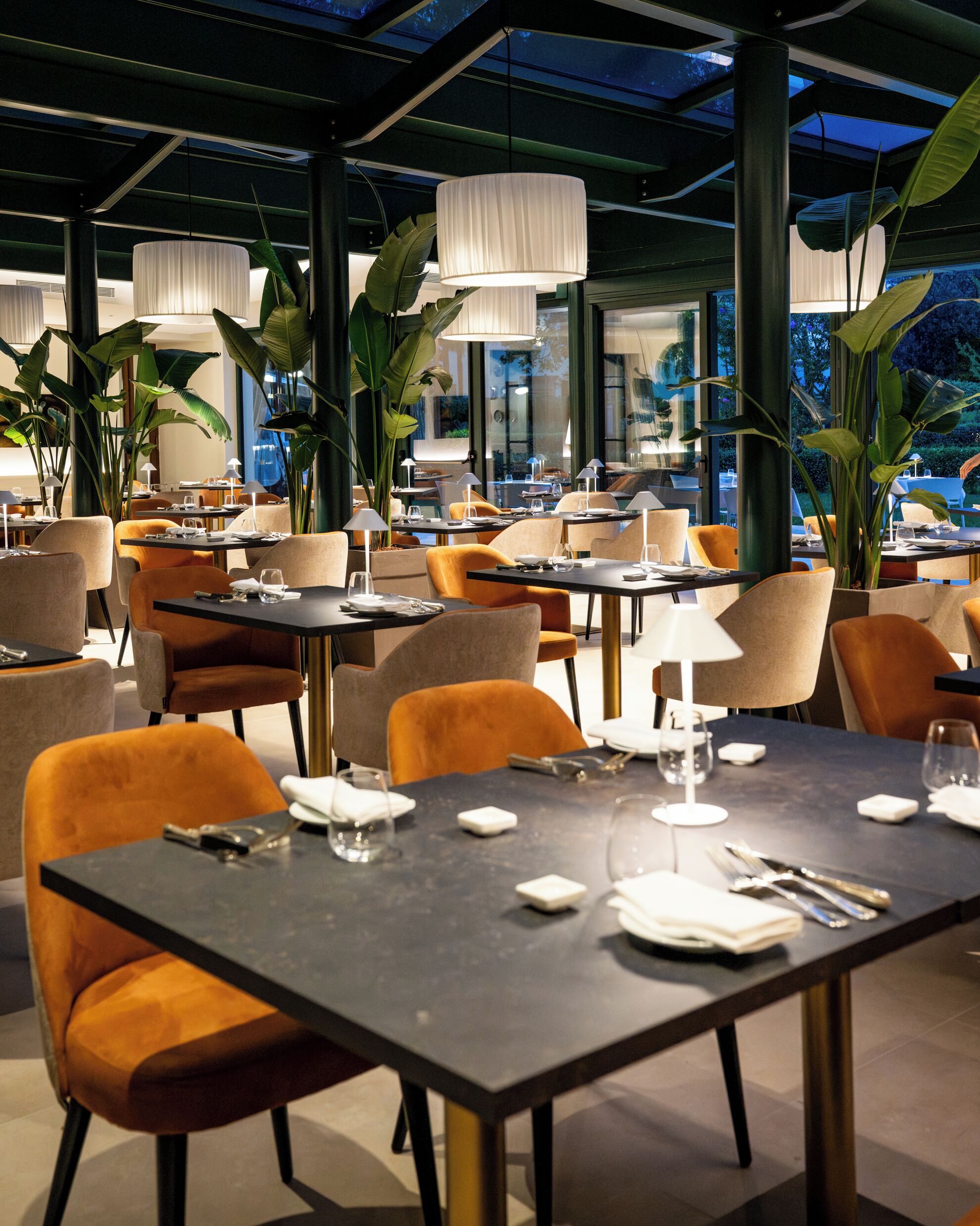 A restaurant with tables and chairs, large windows, and hanging lights.