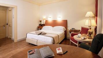Habitación de hotel con cama, mesitas de noche, una mesa redonda con una silla y un libro sobre la mesa.
