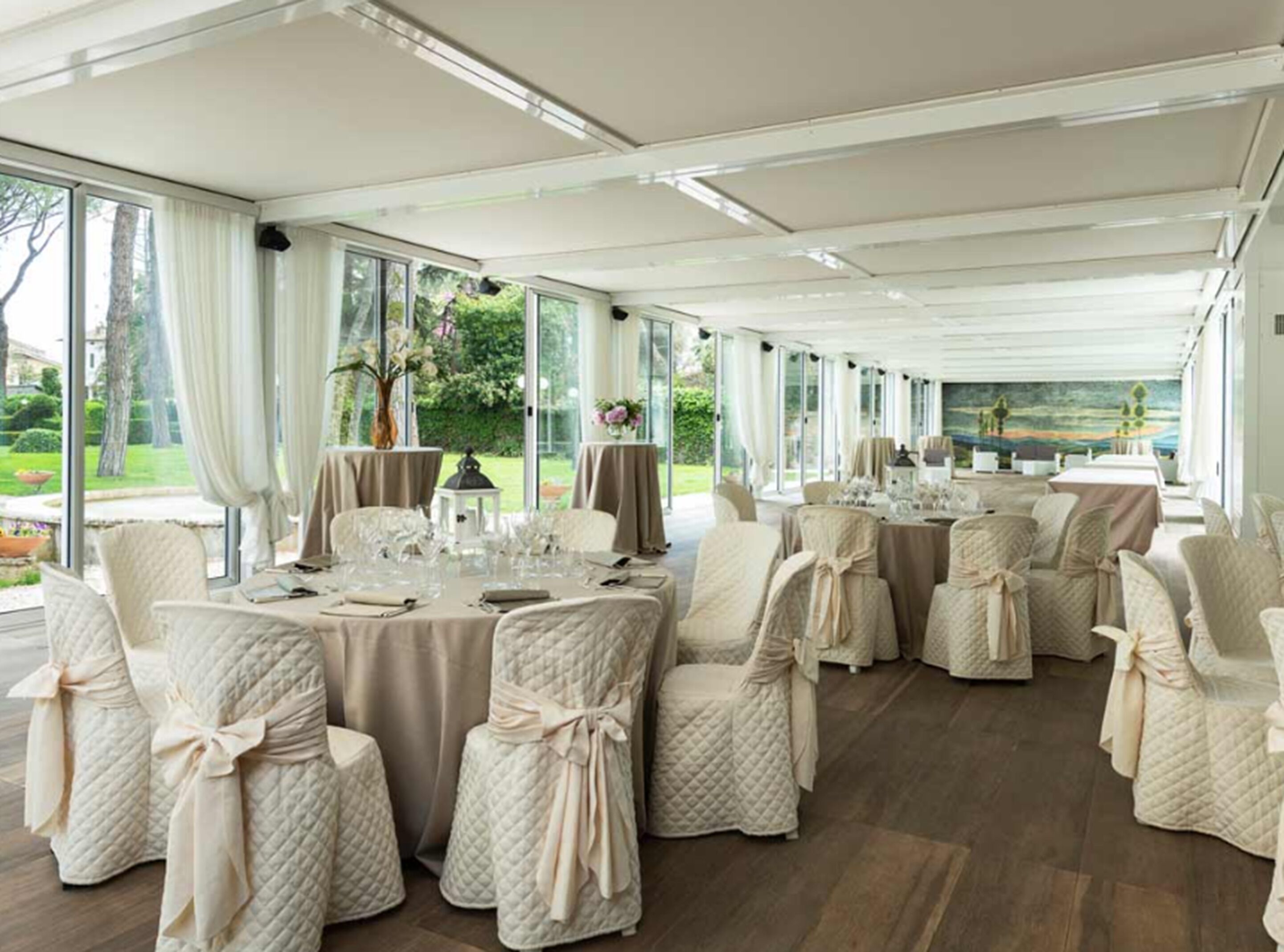 Ein Festsaal mit runden Tischen, Stühlen mit Schleifen und großen Fenstern mit Blick ins Freie.