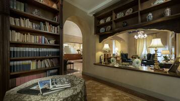 A library with bookshelves, a reading area with a table, and a reception desk with decorative items.