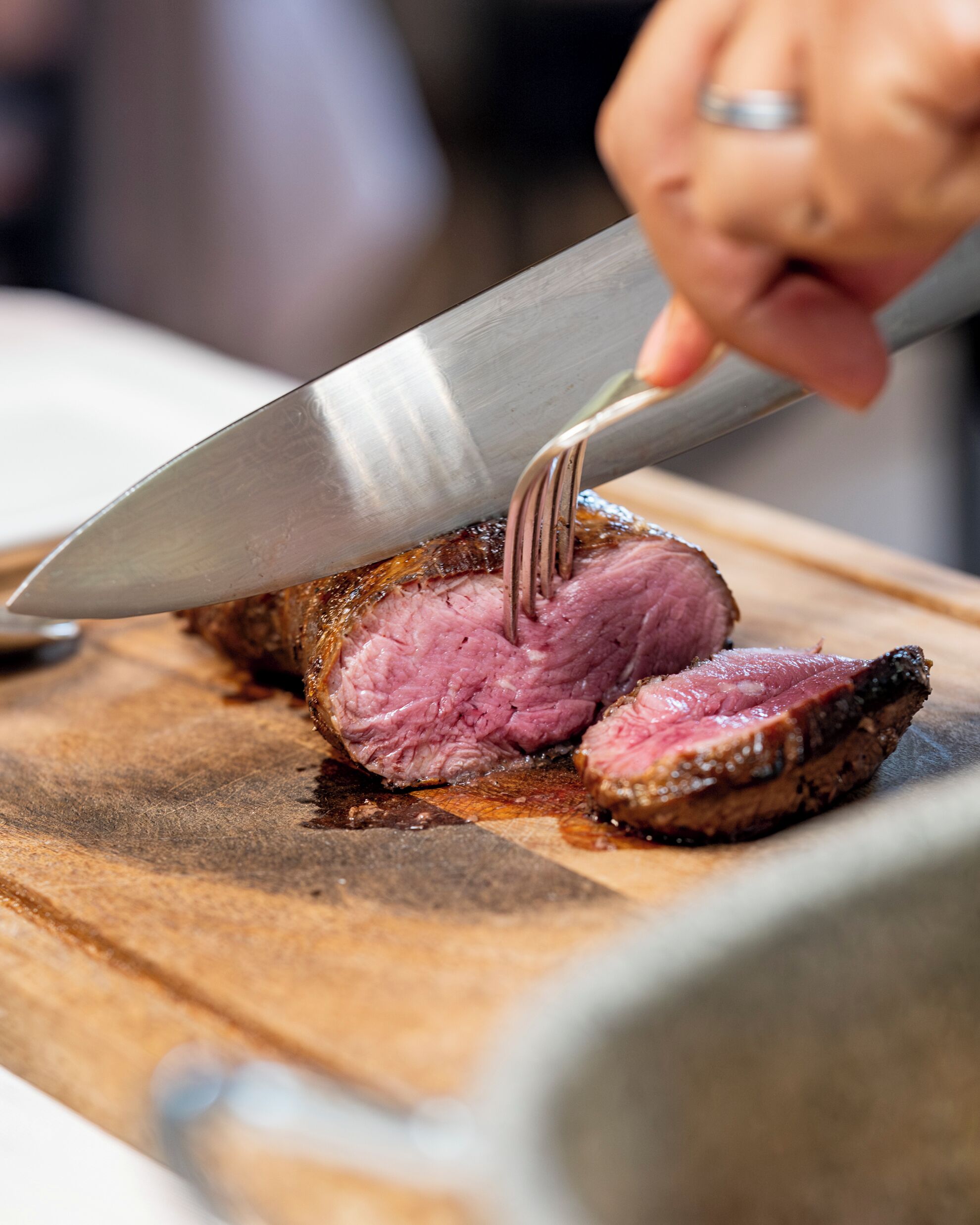 A close-up of a person slicing a cooked meat on a wooden cutting board.
