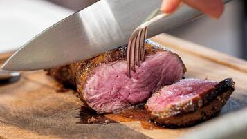 A close-up of a person slicing a cooked meat on a wooden cutting board.