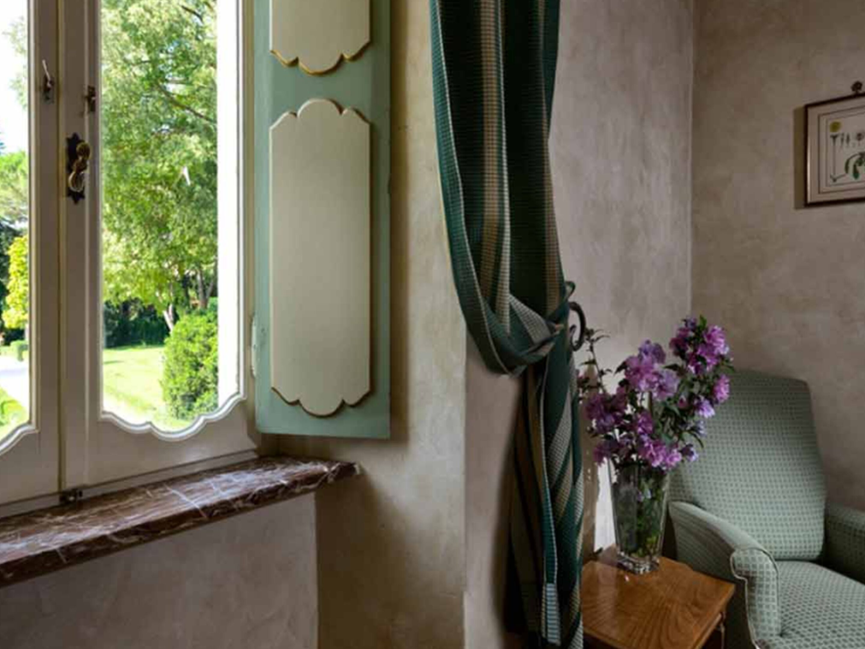 A room with a window, a chair, and a small table with a vase of flowers.