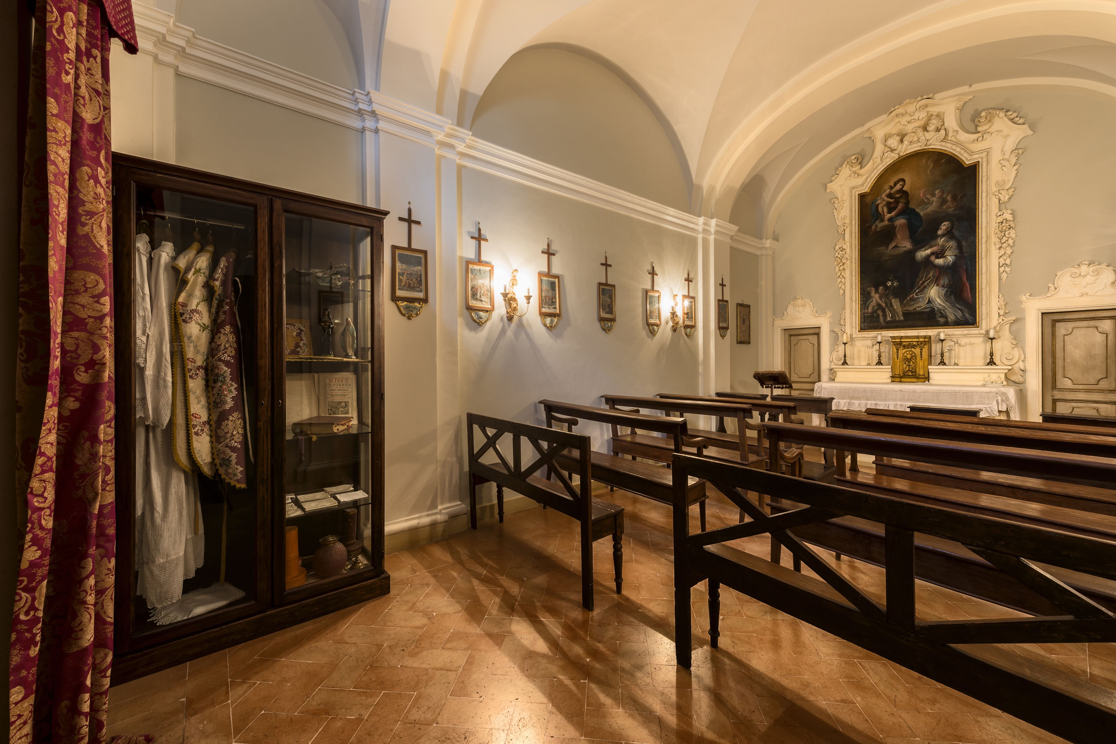 A church interior with wooden pews, a glass display case with religious artifacts, and a large painting above the altar.