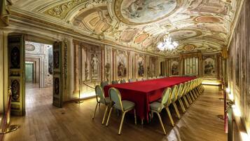 Un gran salón con una larga mesa roja, un techo ornamentado y arte clásico.