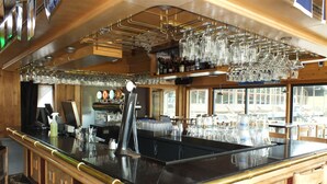 Uma área de bar com balcão preto polido, vários suportes para copos e uma variedade de garrafas e taças.