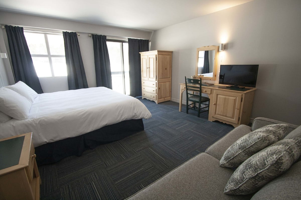 A hotel room with a bed, a desk with a chair, a television, and a wardrobe.
