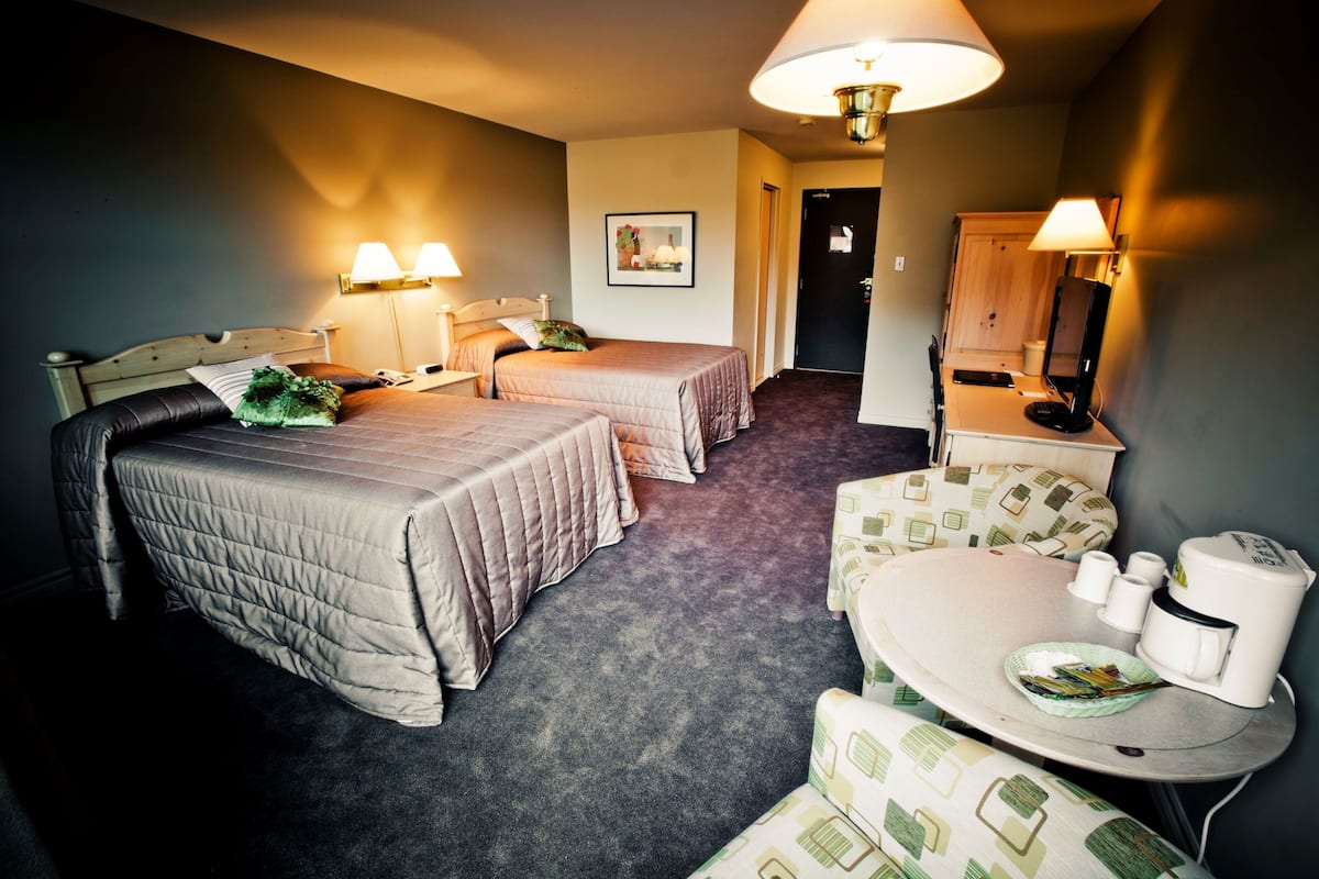 A hotel room with two beds, a small dining area with a table and chairs, and a bathroom visible through an open door.