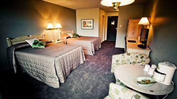 A hotel room with two beds, a small dining area with a table and chairs, and a bathroom visible through an open door.