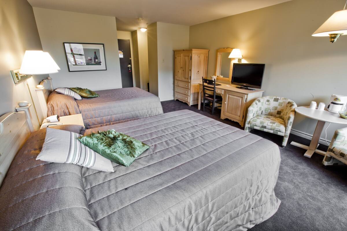 A hotel room with two beds, a desk with a chair, a television, and a coffee machine.