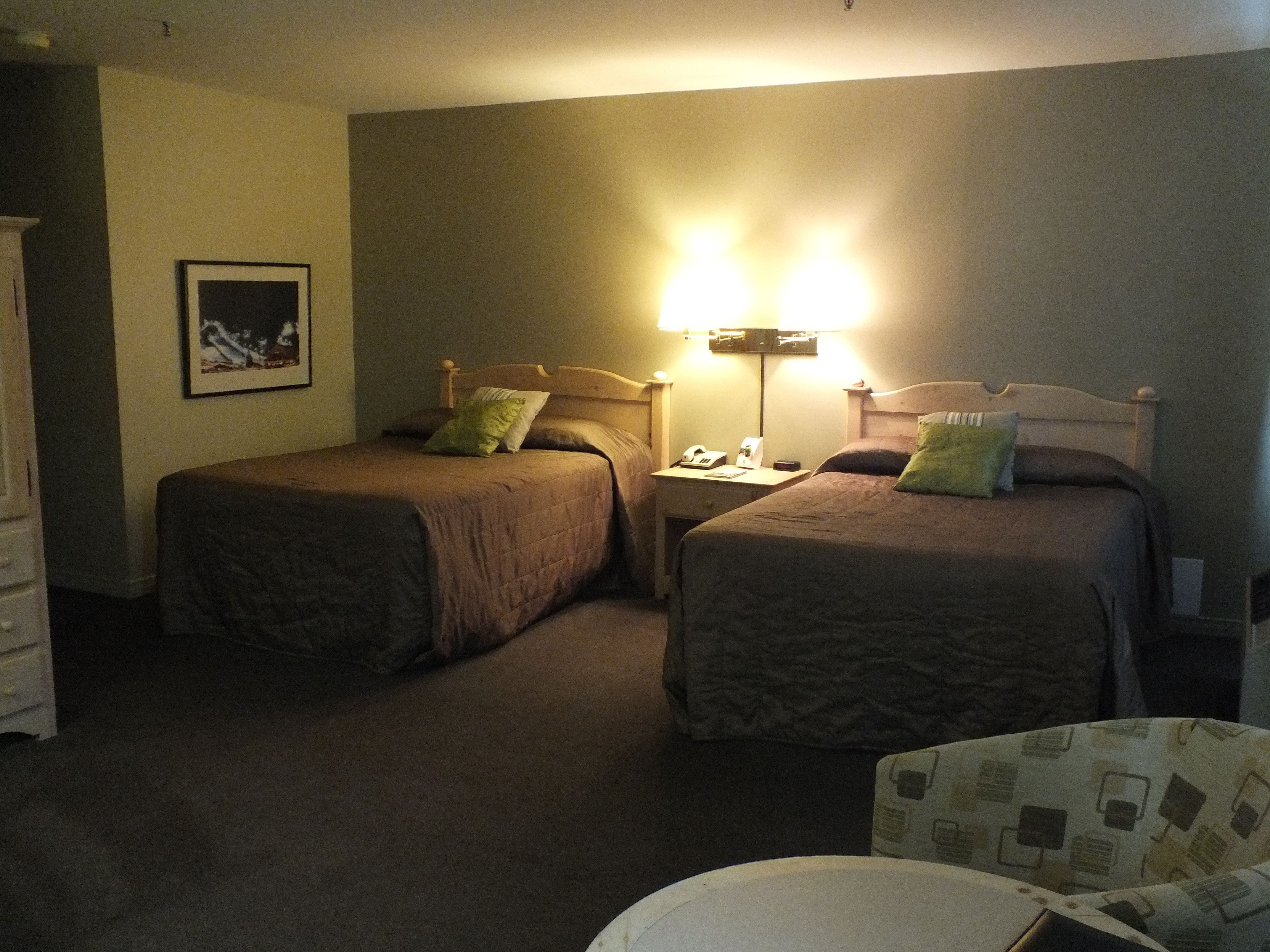 Een hotelkamer met twee eenpersoonsbedden, een nachtkastje met een lamp, een telefoon en een stoel.